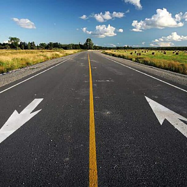 Pista simples de mão dupla: duas setas pintadas no asfalto apontando em sentidos opostos, separadas apenas por uma linha amarela contínua no centro.