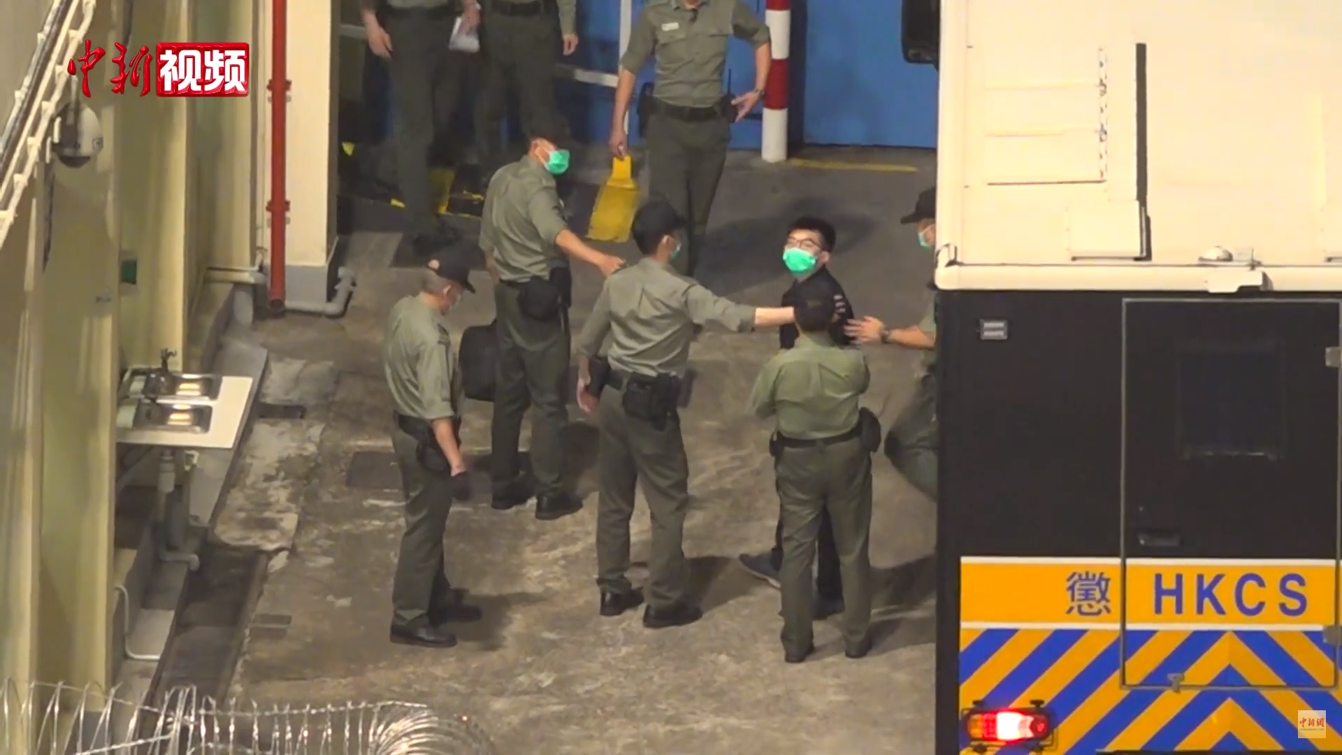 Joshua Wong escoltado por agentes do Departamento de Serviços Correcionais em 2021, no Centro de Recepção de Lai Chi Kok.