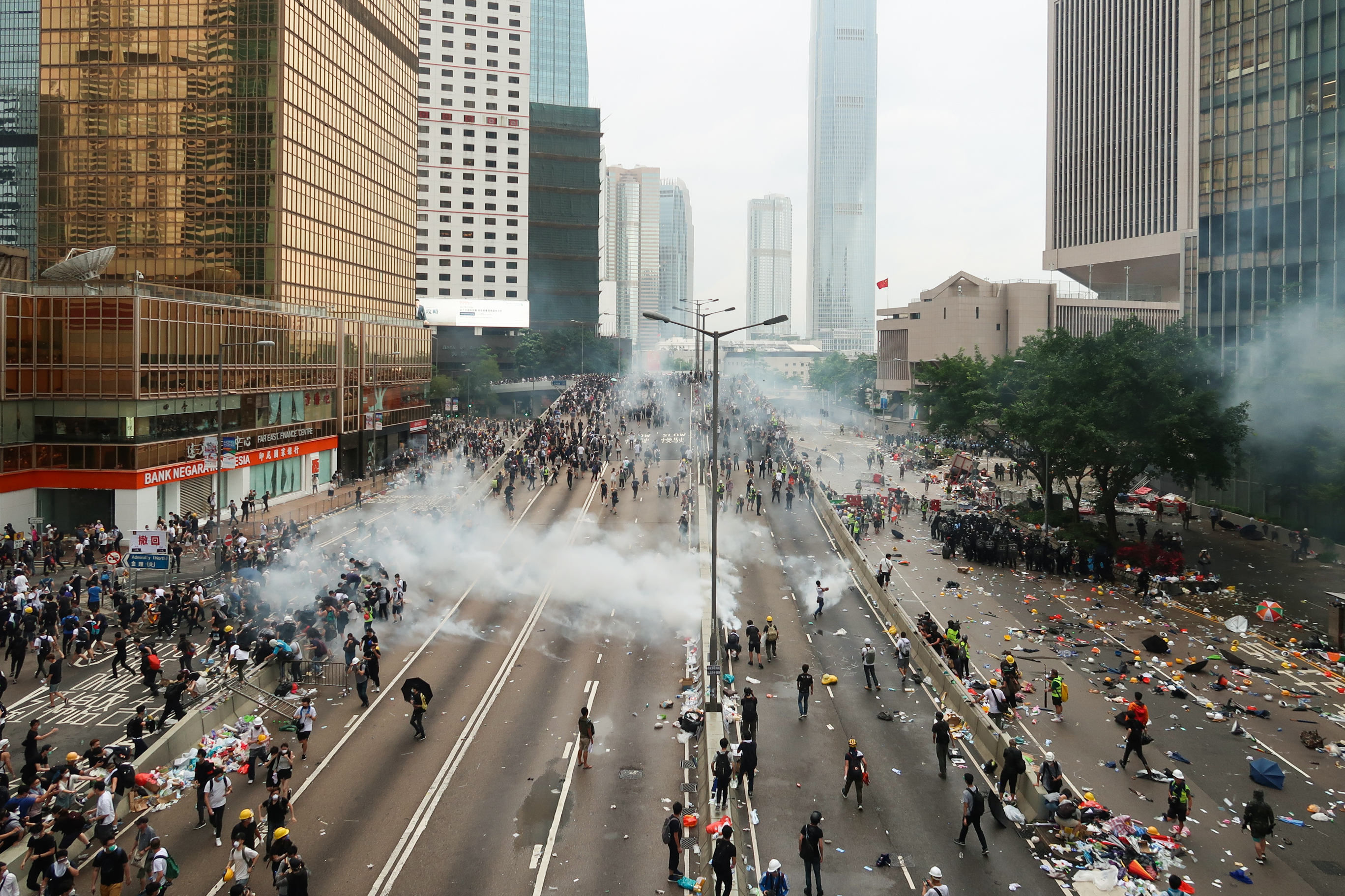 Cena de protesto em 12 de junho de 2019 na Harcourt Road, com fumaça de gás lacrimogêneo dispersando manifestantes.